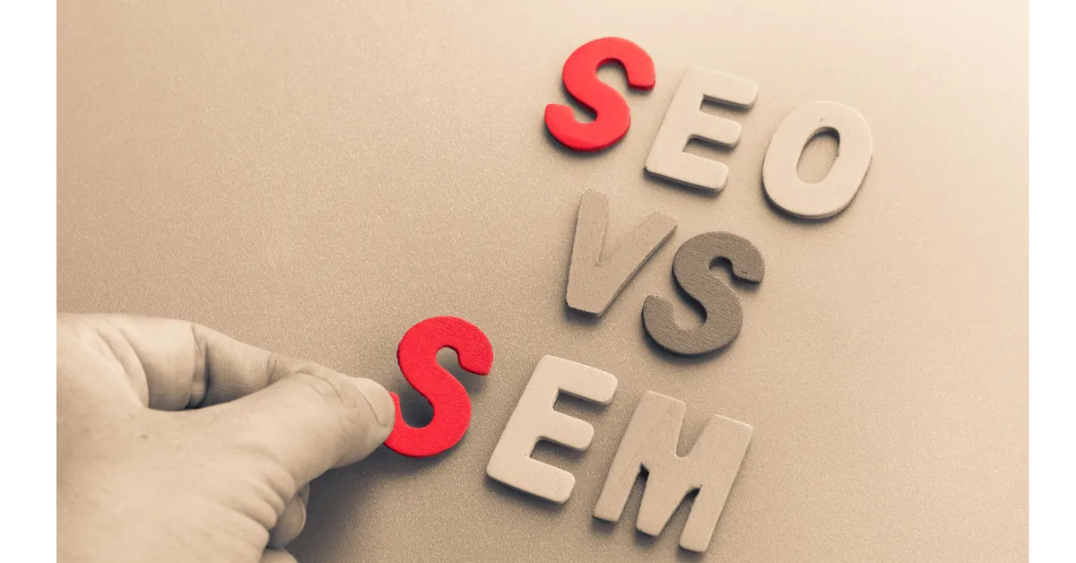 SEO vs SEM comparison showing a hand placing the SEM letter to highlight the difference between organic SEO and paid search marketing.